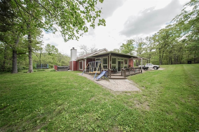 back of house with a sunroom, a chimney, a trampoline, and a lawn