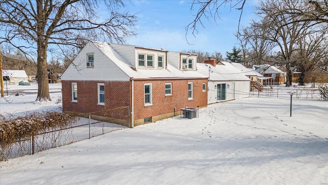 snow covered rear of property with fence and brick siding