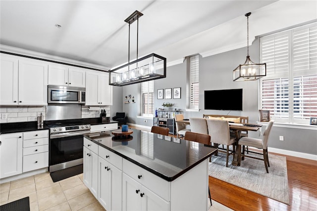 kitchen featuring white cabinetry, crown molding, a center island, pendant lighting, and stainless steel appliances