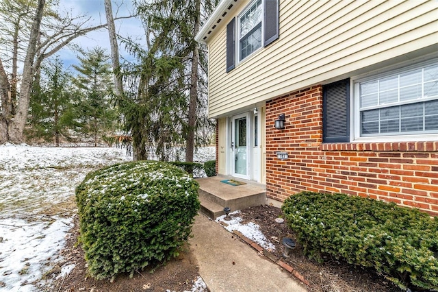 snow covered property entrance featuring brick siding