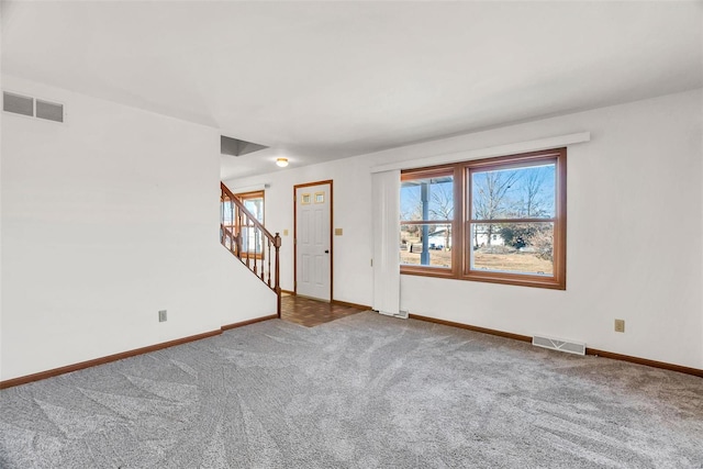 carpeted empty room featuring stairway, visible vents, and baseboards