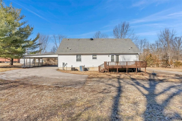 back of house featuring roof with shingles, a deck, a carport, cooling unit, and driveway