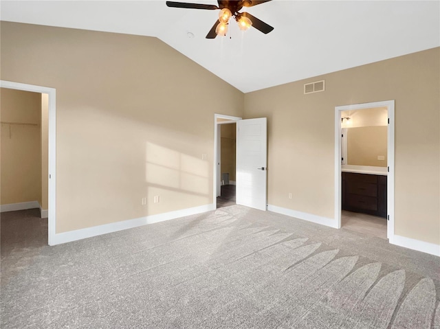 unfurnished bedroom featuring a spacious closet, vaulted ceiling, light carpet, and ensuite bath