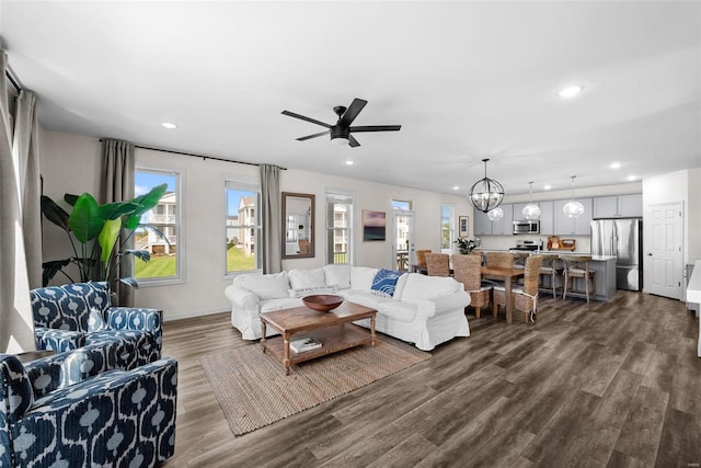 living room with ceiling fan with notable chandelier, baseboards, wood finished floors, and recessed lighting