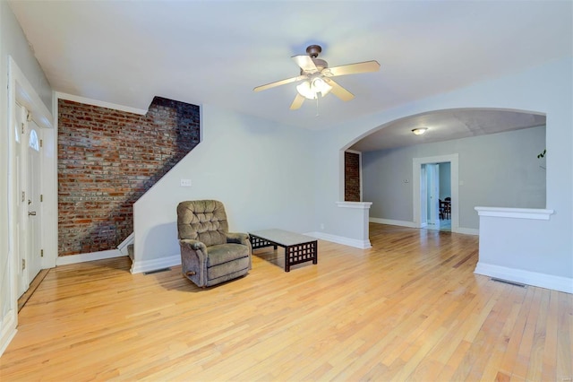 sitting room featuring arched walkways, light wood finished floors, visible vents, brick wall, and baseboards