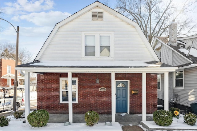 view of front of home with brick siding, covered porch, and a gambrel roof