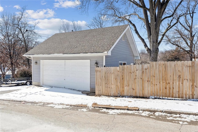 snow covered garage with a garage and fence