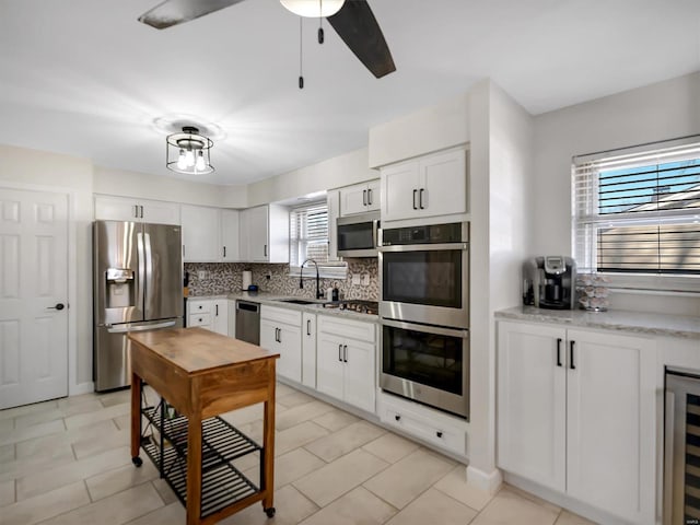 kitchen featuring backsplash, wine cooler, appliances with stainless steel finishes, white cabinetry, and a sink