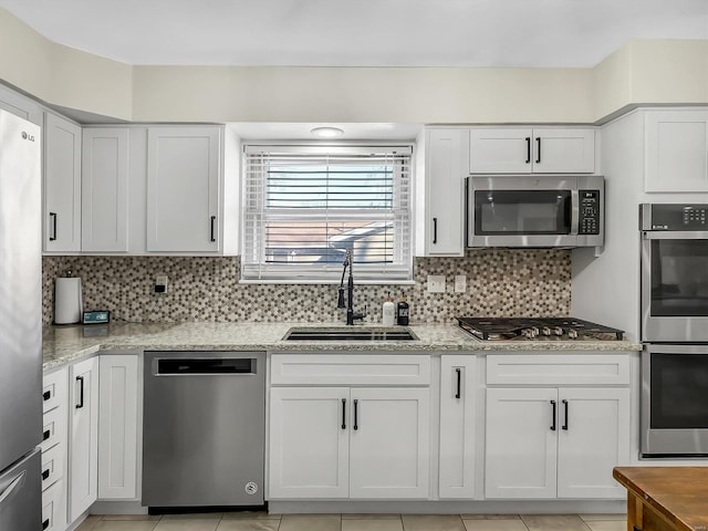 kitchen featuring a sink, light stone counters, tasteful backsplash, white cabinetry, and appliances with stainless steel finishes