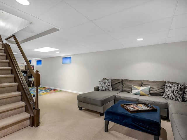 living area featuring a drop ceiling, baseboards, light carpet, and stairs