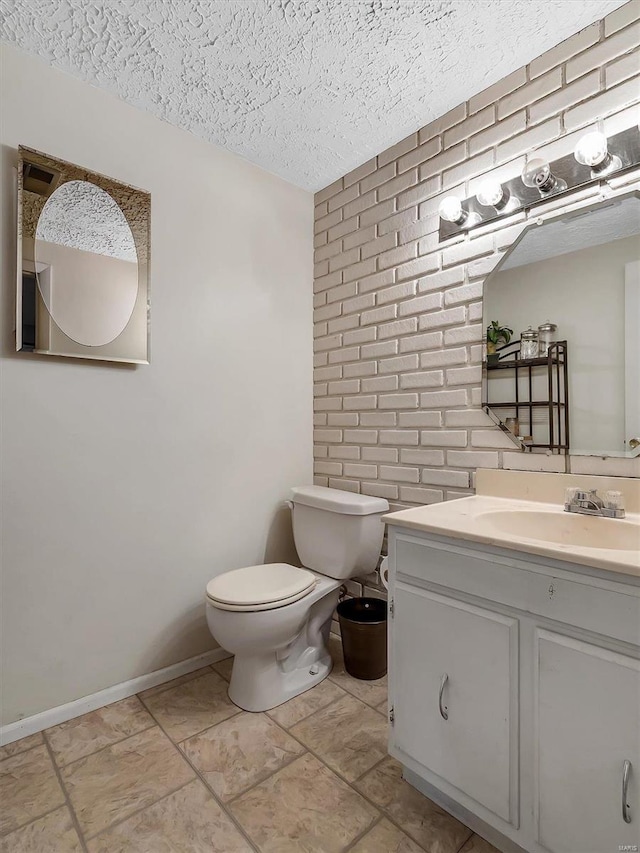 half bathroom featuring toilet, a textured ceiling, brick wall, baseboards, and vanity