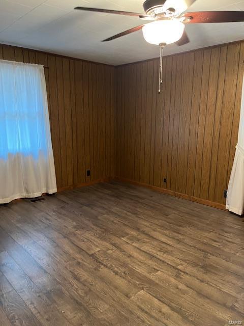 empty room with dark hardwood / wood-style flooring, ceiling fan, and wood walls