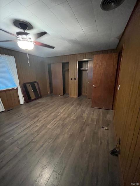 unfurnished living room featuring ceiling fan, wooden walls, and dark hardwood / wood-style flooring