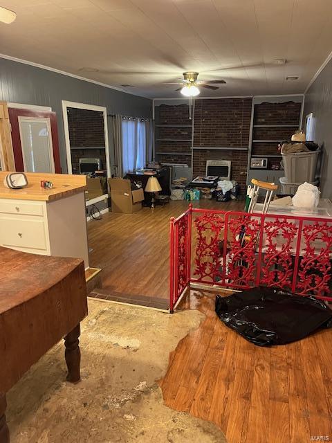 interior space featuring ceiling fan, ornamental molding, wood-type flooring, and a brick fireplace