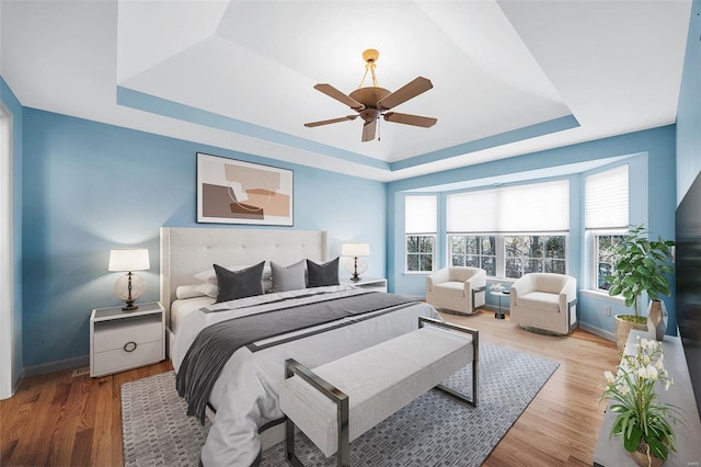 bedroom featuring ceiling fan, a tray ceiling, wood finished floors, and baseboards