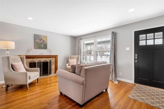 living room featuring baseboards, a fireplace with raised hearth, wood finished floors, and recessed lighting