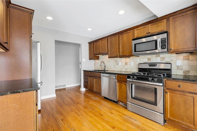 kitchen featuring decorative backsplash, light wood finished floors, a sink, appliances with stainless steel finishes, and brown cabinetry