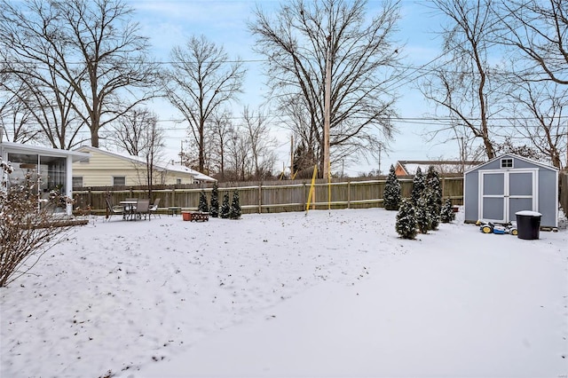 snowy yard featuring a fenced backyard, an outbuilding, and a storage unit