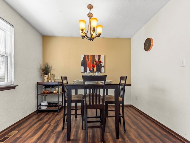 dining room with dark wood-type flooring, a notable chandelier, a textured wall, and visible vents