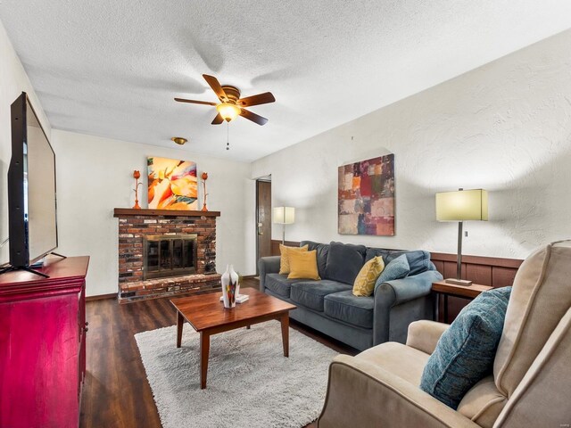 living area with a brick fireplace, wood finished floors, a textured wall, a textured ceiling, and a ceiling fan