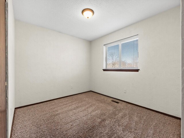 empty room featuring visible vents, baseboards, carpet floors, a textured wall, and a textured ceiling