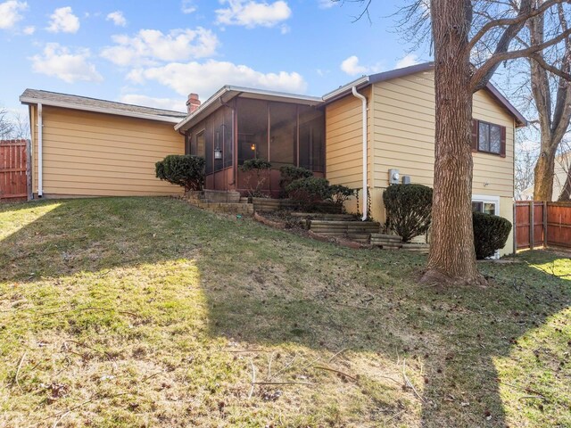 back of house featuring fence, a chimney, a lawn, and a sunroom