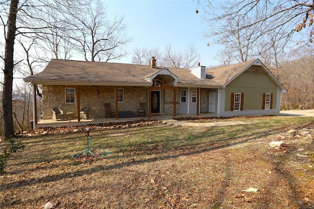 view of front facade with stone siding, covered porch, a chimney, and a front yard