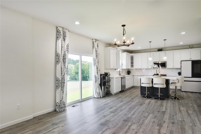 kitchen featuring a center island, decorative light fixtures, appliances with stainless steel finishes, white cabinets, and a kitchen bar