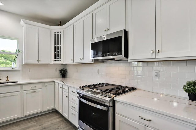 kitchen with appliances with stainless steel finishes, light stone counters, light hardwood / wood-style floors, white cabinets, and decorative backsplash