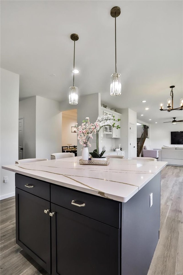 kitchen featuring hardwood / wood-style flooring, pendant lighting, a center island, and light stone counters