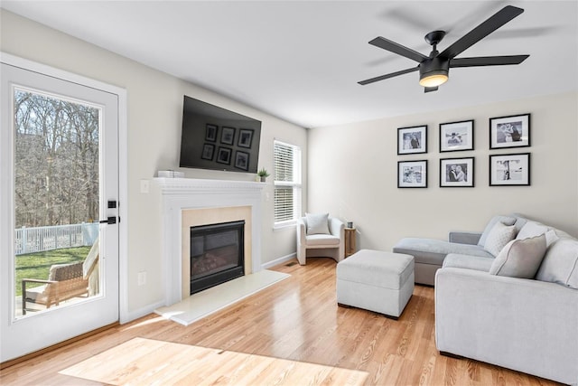 living room featuring a ceiling fan, wood finished floors, baseboards, and a high end fireplace