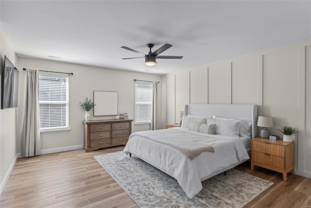 bedroom featuring visible vents, light wood finished floors, a ceiling fan, a decorative wall, and baseboards