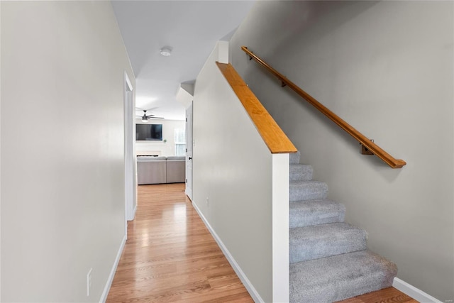 stairs with wood finished floors, baseboards, and ceiling fan