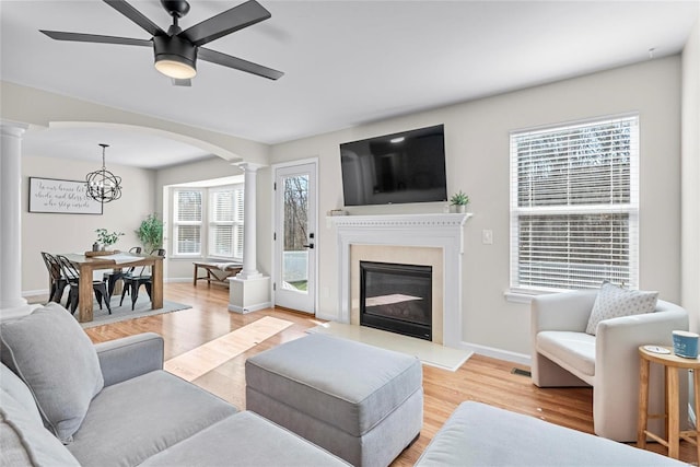 living area featuring a glass covered fireplace, light wood-type flooring, ornate columns, and ceiling fan