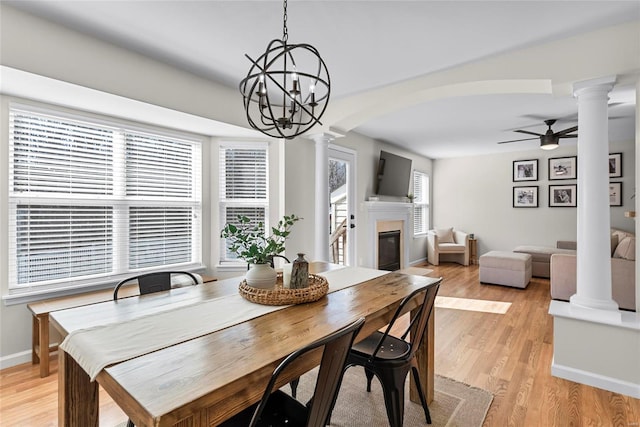 dining space with a ceiling fan, decorative columns, arched walkways, a glass covered fireplace, and light wood-type flooring