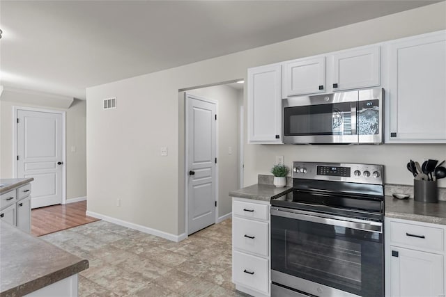 kitchen with dark countertops, visible vents, baseboards, appliances with stainless steel finishes, and white cabinetry