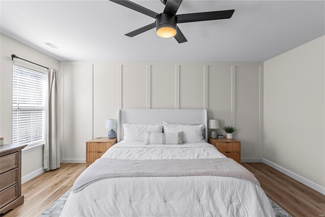 bedroom with light wood-type flooring, baseboards, a ceiling fan, and a decorative wall