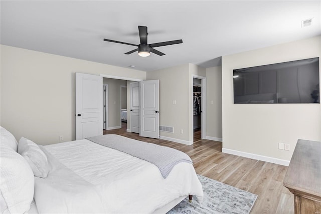 bedroom with a walk in closet, light wood-style flooring, baseboards, and visible vents