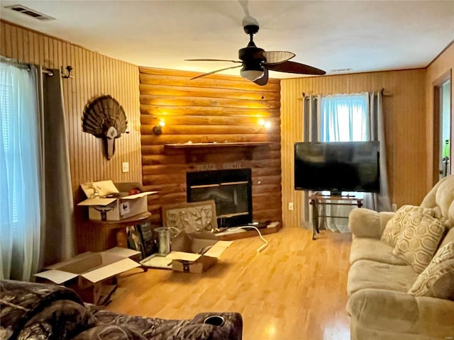 living room with hardwood / wood-style floors, ceiling fan, a large fireplace, and log walls