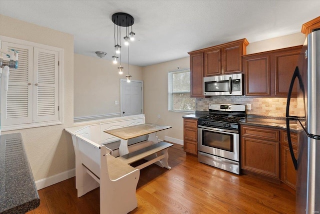 kitchen featuring wood-type flooring, decorative backsplash, stainless steel appliances, and decorative light fixtures