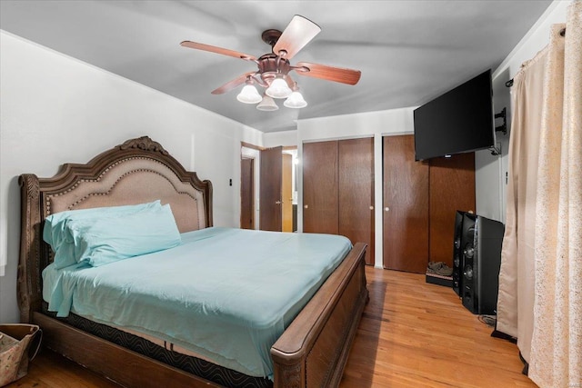 bedroom with light wood finished floors, two closets, and ceiling fan