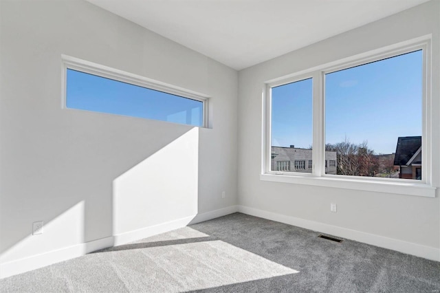 carpeted spare room featuring a wealth of natural light, visible vents, and baseboards