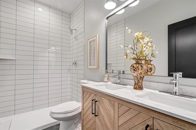 bathroom featuring a sink, a tile shower, toilet, and double vanity