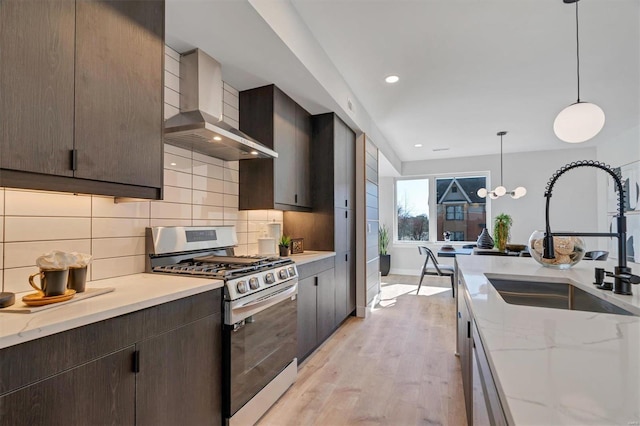 kitchen featuring wall chimney exhaust hood, appliances with stainless steel finishes, light stone counters, decorative light fixtures, and a sink