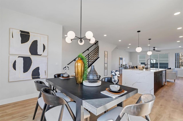 dining space with stairs, light wood finished floors, recessed lighting, baseboards, and ceiling fan with notable chandelier