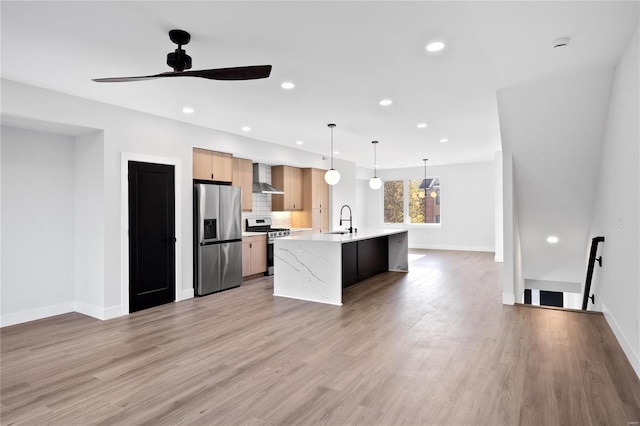 kitchen featuring sink, stainless steel appliances, wall chimney exhaust hood, light brown cabinetry, and hanging light fixtures