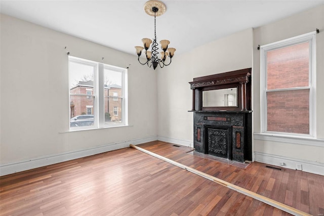 unfurnished living room with a notable chandelier, wood finished floors, a fireplace with flush hearth, baseboards, and visible vents