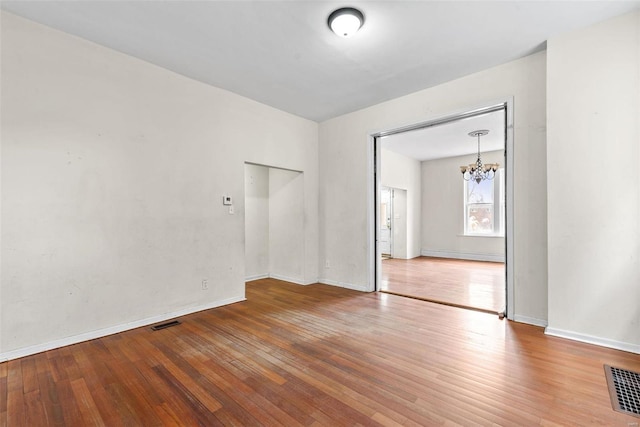 spare room featuring a chandelier, visible vents, baseboards, and wood finished floors