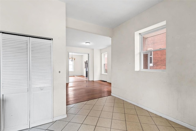 corridor with an inviting chandelier, baseboards, and light tile patterned floors