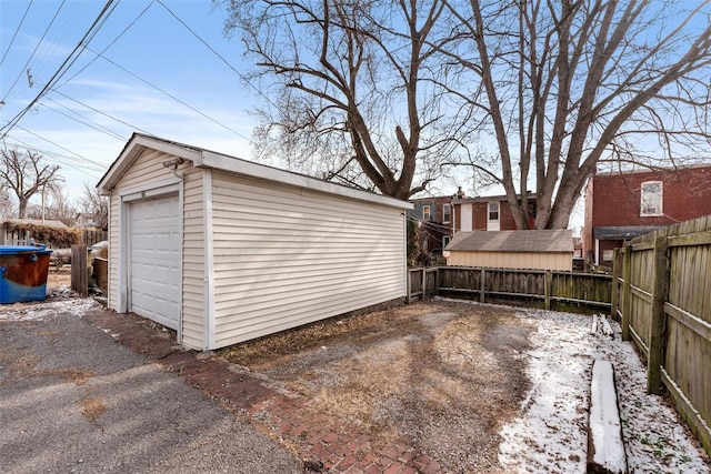 snow covered garage featuring a garage, fence, and aphalt driveway